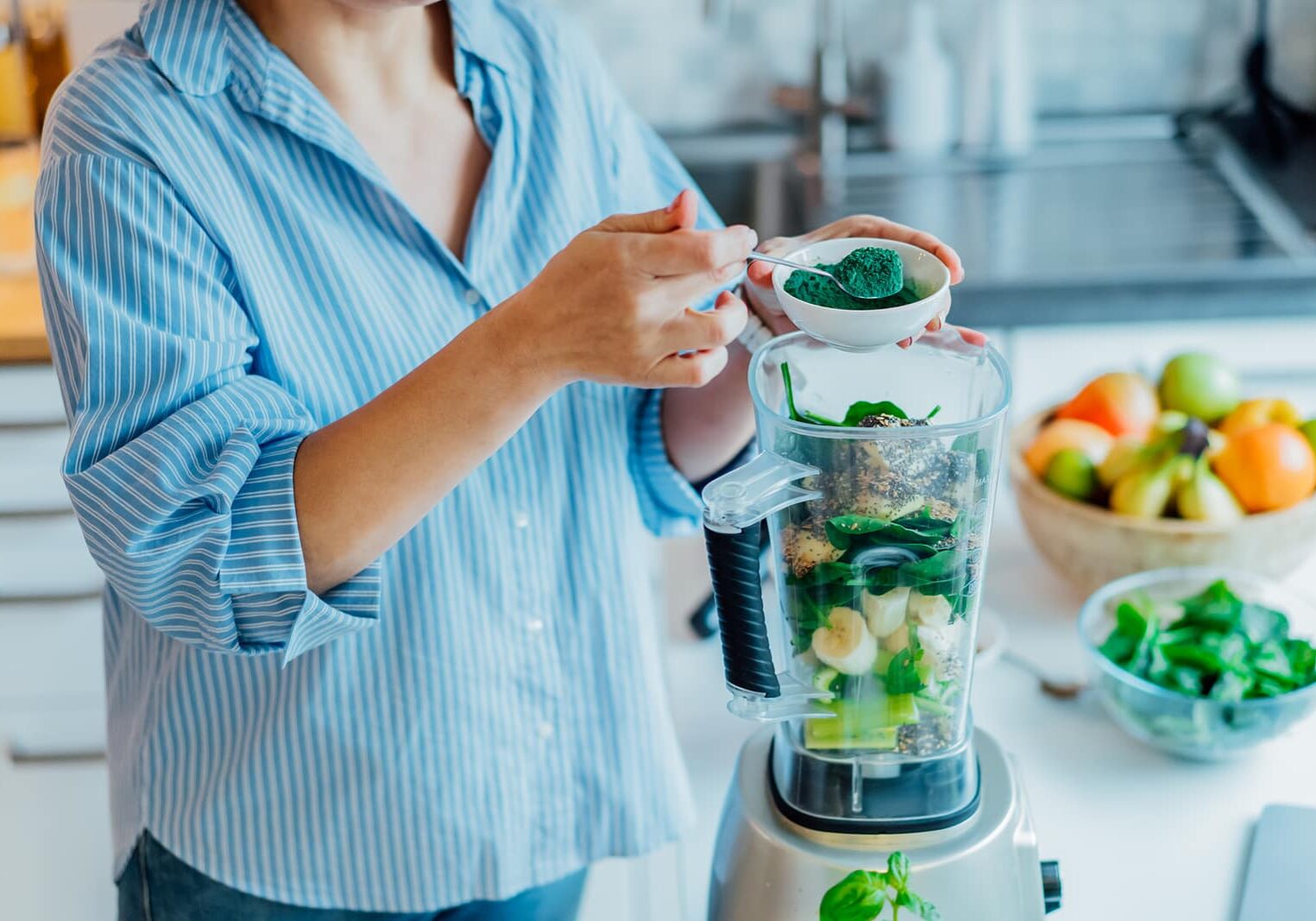 Woman adding spirulina green powder during making green smoothie on the kitchen. Superfood supplement. Healthy detox vegan diet. Healthy dieting eating, weight loss program. Selective focus.